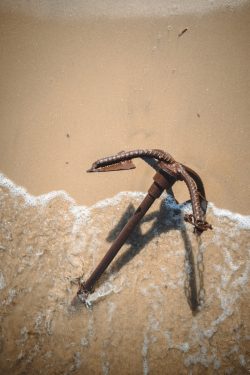 a rusty anchor laying on the sand of a beach